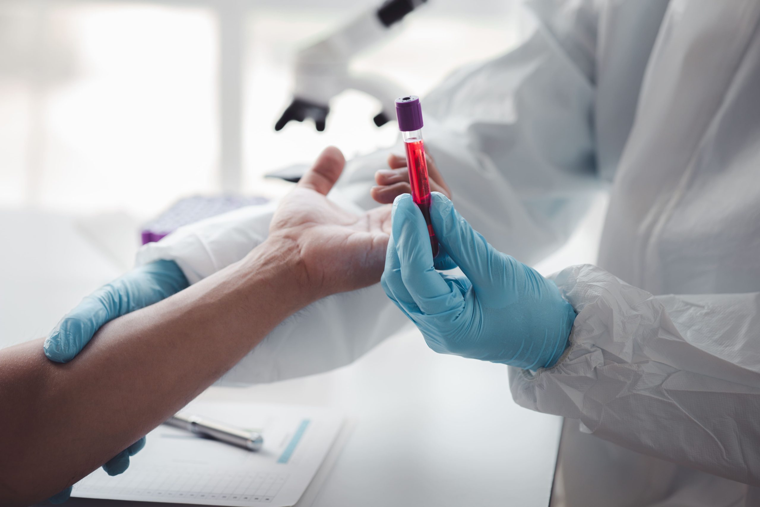 A healthcare professional in gloves holding a blood sample vial while preparing for testing on a patient's arm.