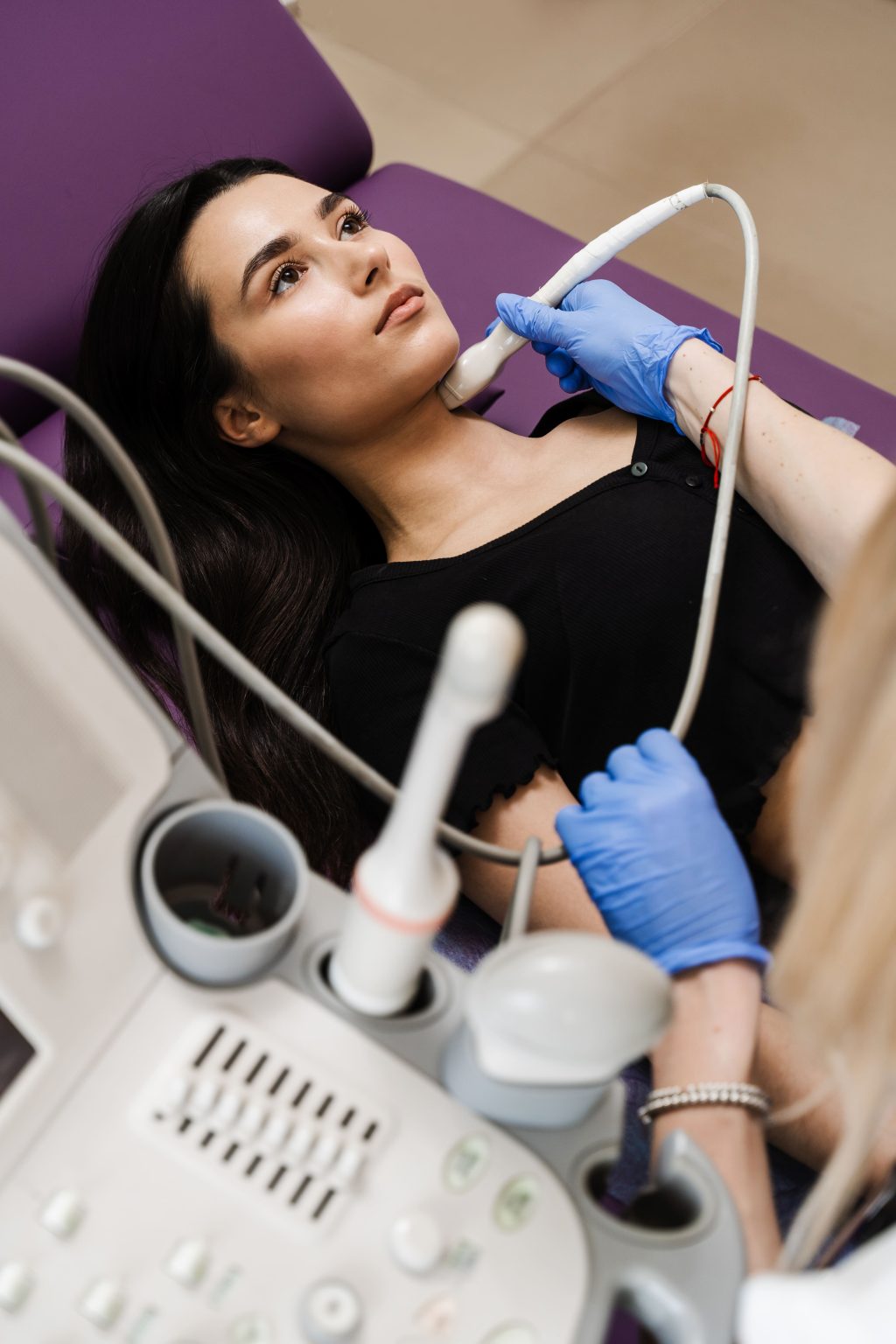 A young woman undergoing a thyroid ultrasound in a clinic setting.